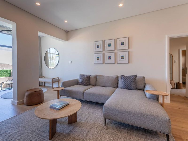 A bright and modern living room featuring high-quality timber flooring, recessed lighting, and seamless access to an outdoor patio area.