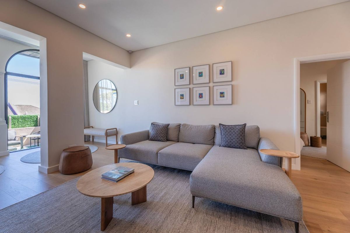 A bright and modern living room featuring high-quality timber flooring, recessed lighting, and seamless access to an outdoor patio area.