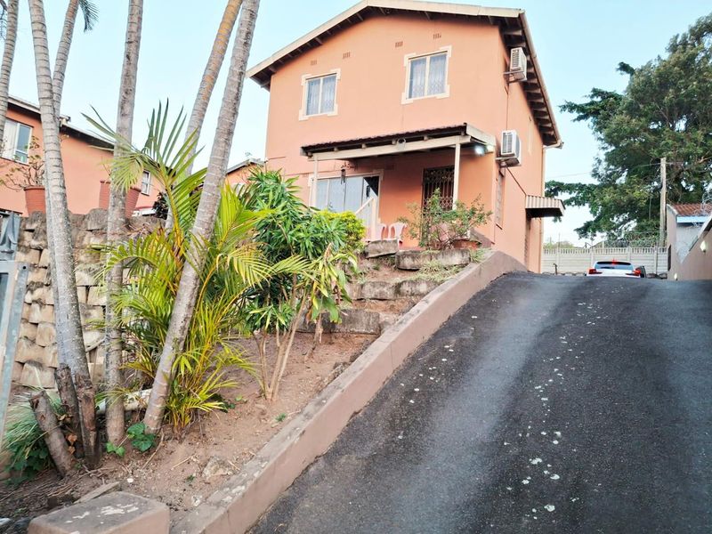 Front exterior view of a two-story house featuring an asphalt driveway, retaining wall, and a covered entrance porch.