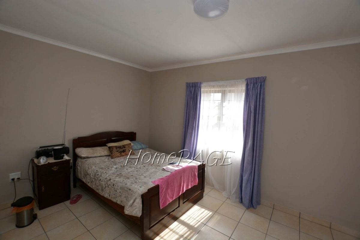 A standard bedroom featuring tiled flooring, neutral wall paint, and a window with curtain tracks.