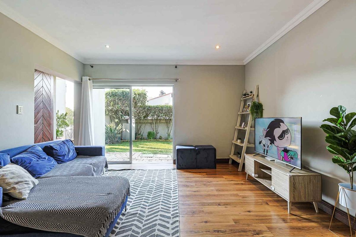 Bright living room featuring warm hardwood flooring, crown molding, and large sliding glass doors providing direct access to the rear garden.