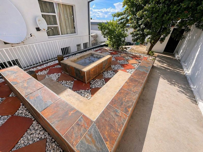 Outdoor entertainment area featuring a built-in tiled fire pit and integrated seating, set within a landscaped courtyard with pebble and tile accents.