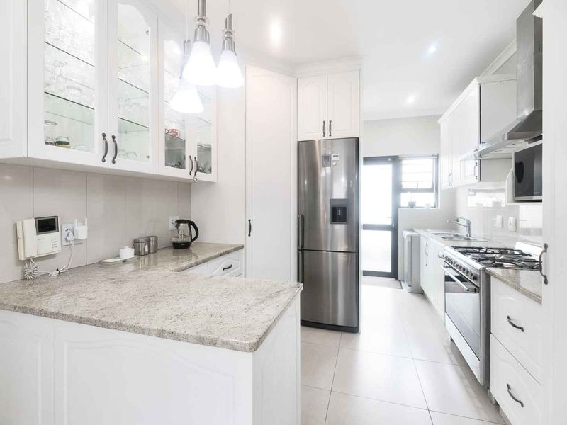 Modern kitchen featuring white cabinetry, granite countertops, stainless steel appliances, and tiled flooring with ample storage and workspace.