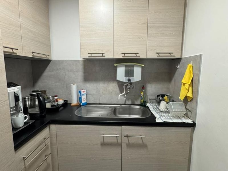 Compact kitchenette featuring light wood-grain cabinetry, a stainless steel sink, tiled backsplash, and a built-in water filtration unit.