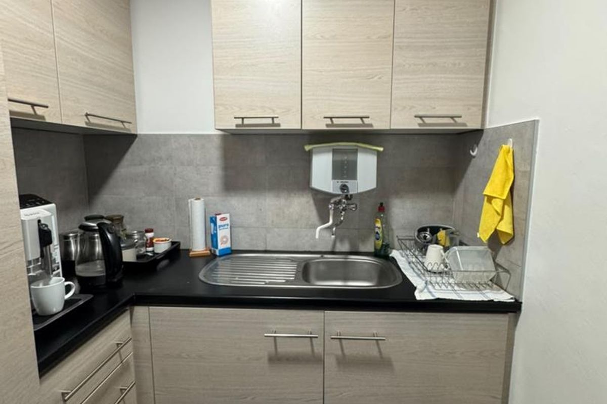 Compact kitchenette featuring light wood-grain cabinetry, a stainless steel sink, tiled backsplash, and a built-in water filtration unit.