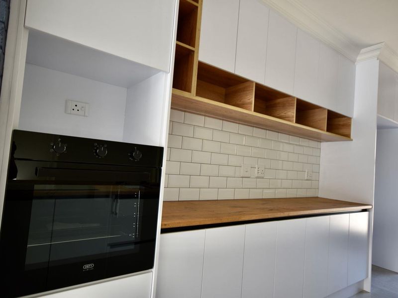Modern kitchen featuring white cabinetry, wooden countertops, open shelving, and a subway tile backsplash with a built-in oven.
