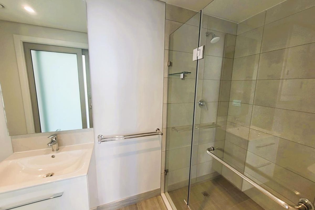 Modern bathroom featuring a glass-enclosed walk-in shower, wall-mounted vanity with integrated basin, and neutral floor-to-ceiling tiling.