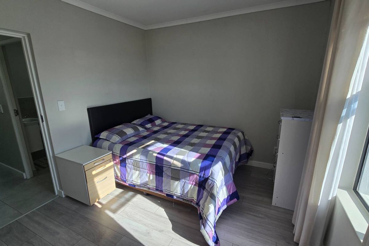 A well-lit bedroom featuring modern laminate flooring and neutral wall tones, providing a clean and functional living space.