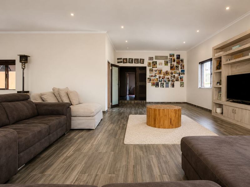 Spacious living room featuring wood-look tile flooring, recessed ceiling lighting, and a large built-in wooden shelving unit for media and display.