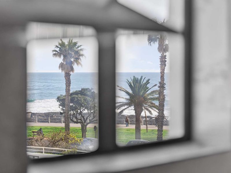 A scenic view of the ocean, coastal promenade, and palm trees captured through a window frame.