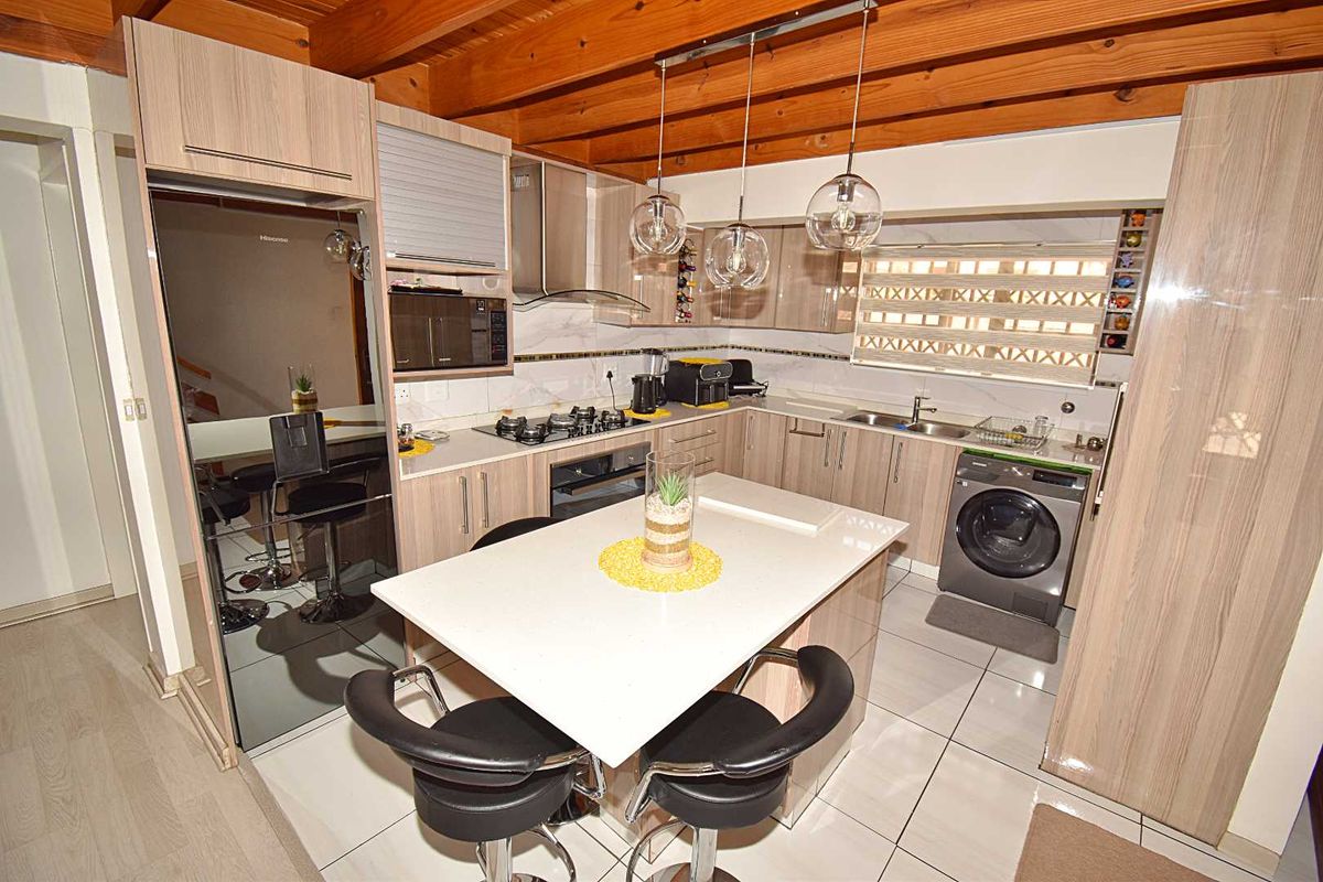 Modern kitchen featuring light wood cabinetry, stone countertops, a central island, built-in gas hob, oven, extractor fan, and integrated laundry appliance.