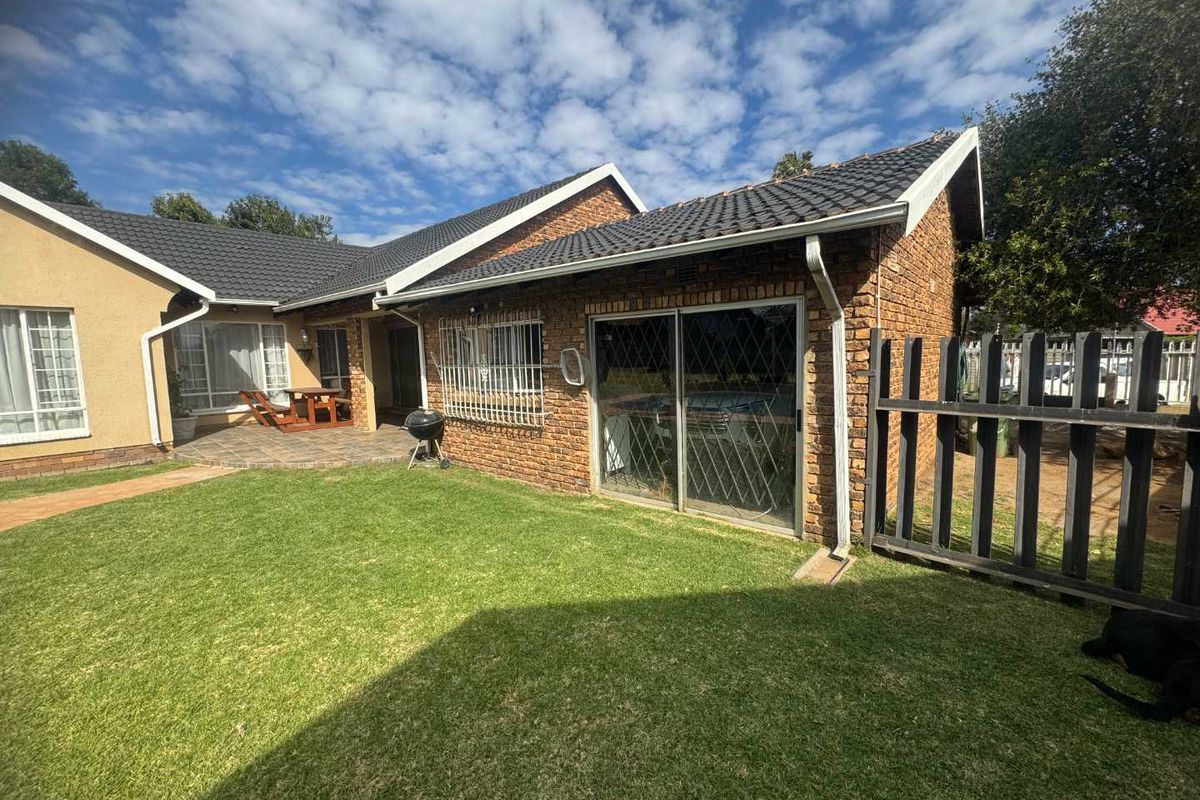 Rear view of the house featuring a brick facade, tiled roof, sliding glass doors with security bars, and a well-maintained lawn.