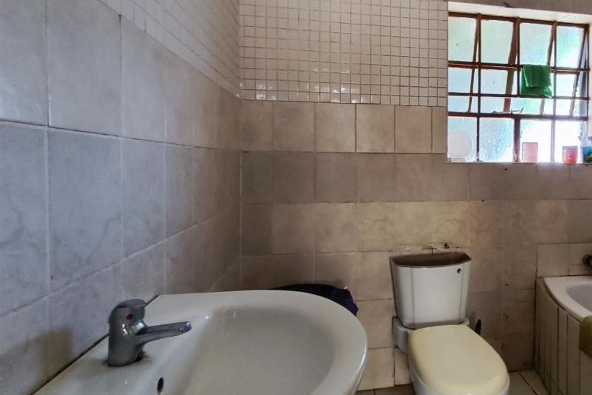A dated bathroom featuring a pedestal basin, standard toilet, and tiled walls with a window providing natural light.