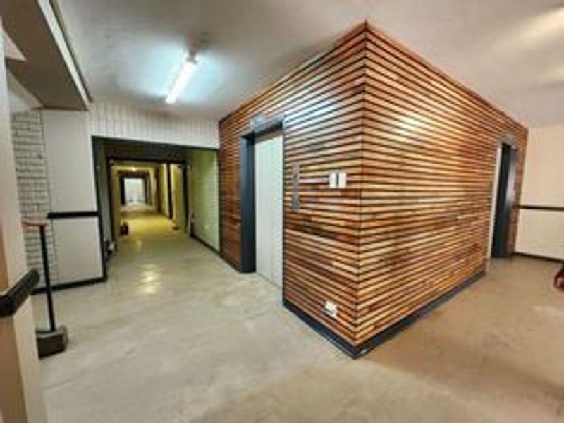 A communal apartment hallway featuring a prominent timber-slatted elevator lobby and access to a long corridor with basic finishes.