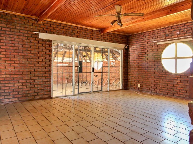 Spacious living area featuring exposed brick walls, timber ceiling, ceramic tiled flooring, and a unique circular window with access to an outdoor area.