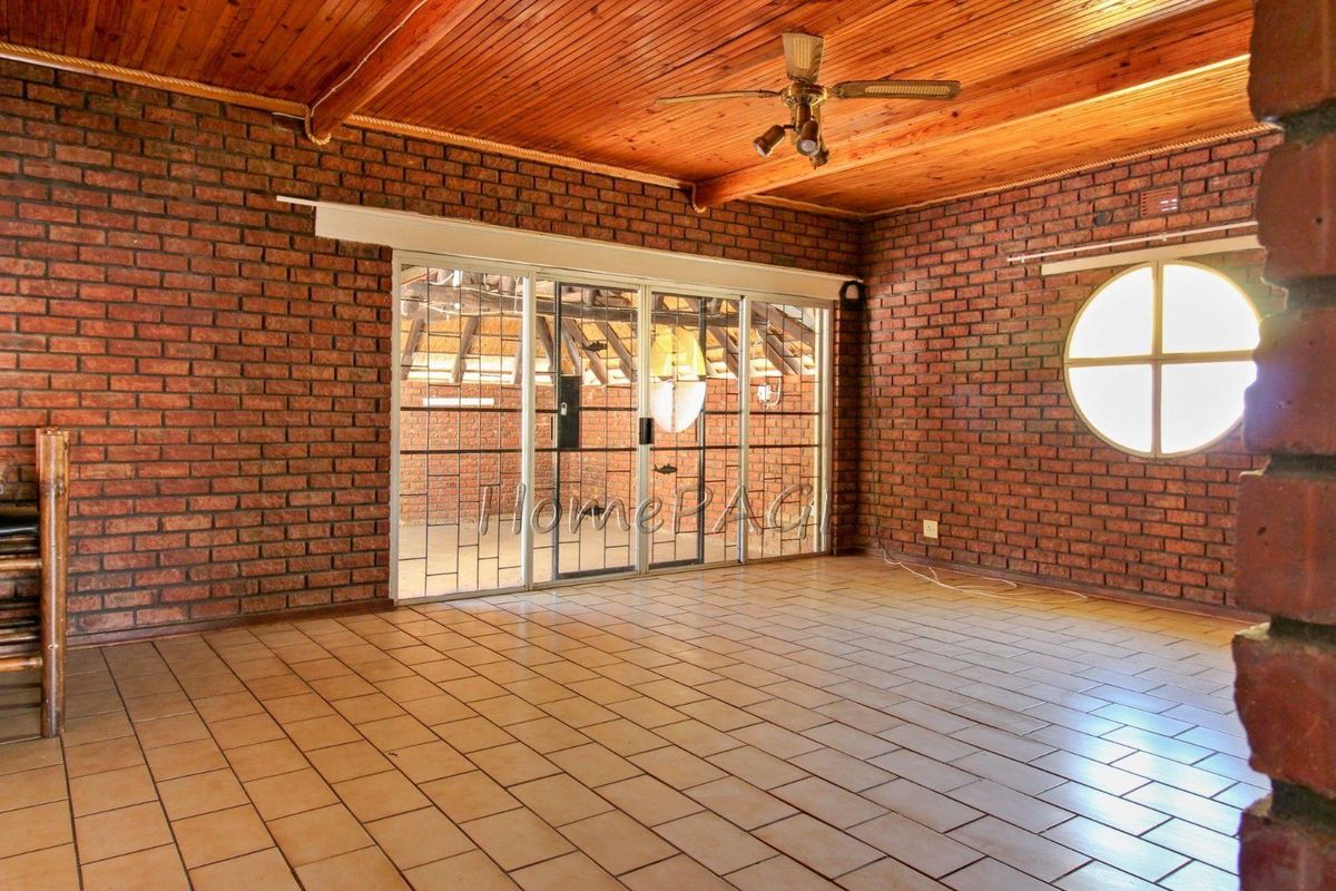 Spacious living area featuring exposed brick walls, timber ceiling, ceramic tiled flooring, and a unique circular window with access to an outdoor area.