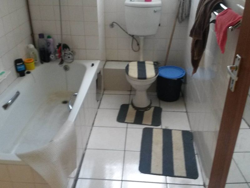 A dated bathroom featuring a standard bathtub, toilet, and white wall tiles. The space requires cosmetic updates to improve its overall condition.