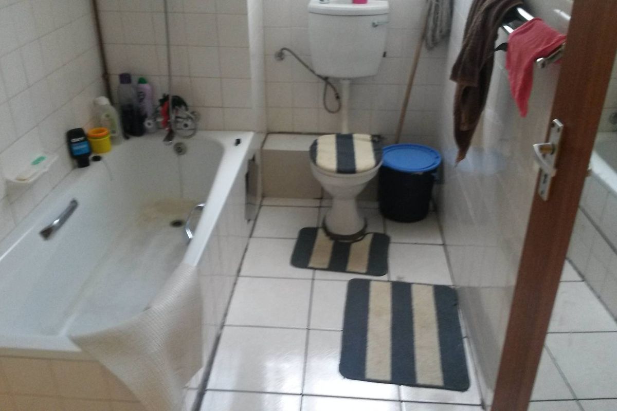 A dated bathroom featuring a standard bathtub, toilet, and white wall tiles. The space requires cosmetic updates to improve its overall condition.