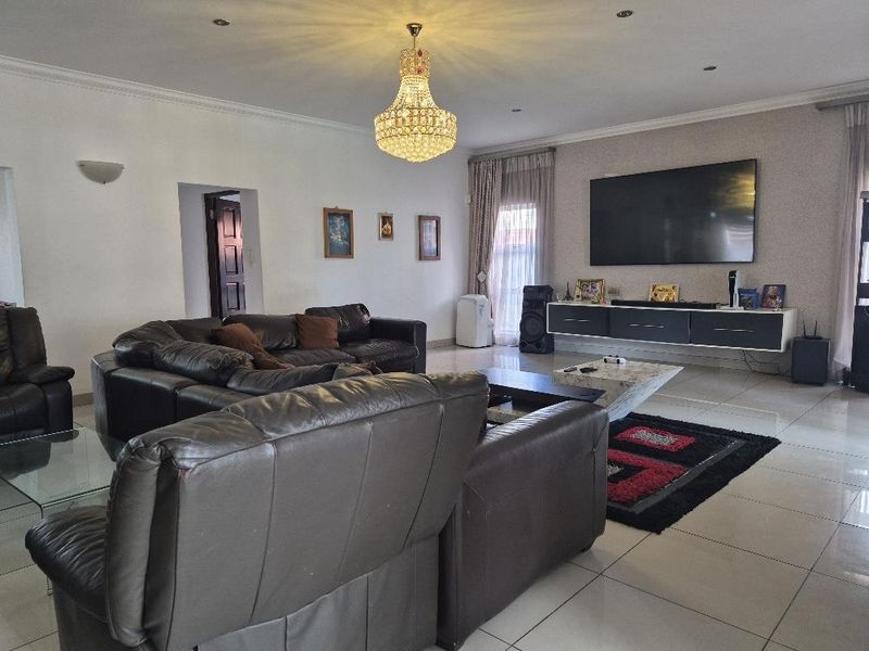 Spacious living room featuring tiled flooring, recessed downlights, a decorative crystal chandelier, and a modern floating media console.