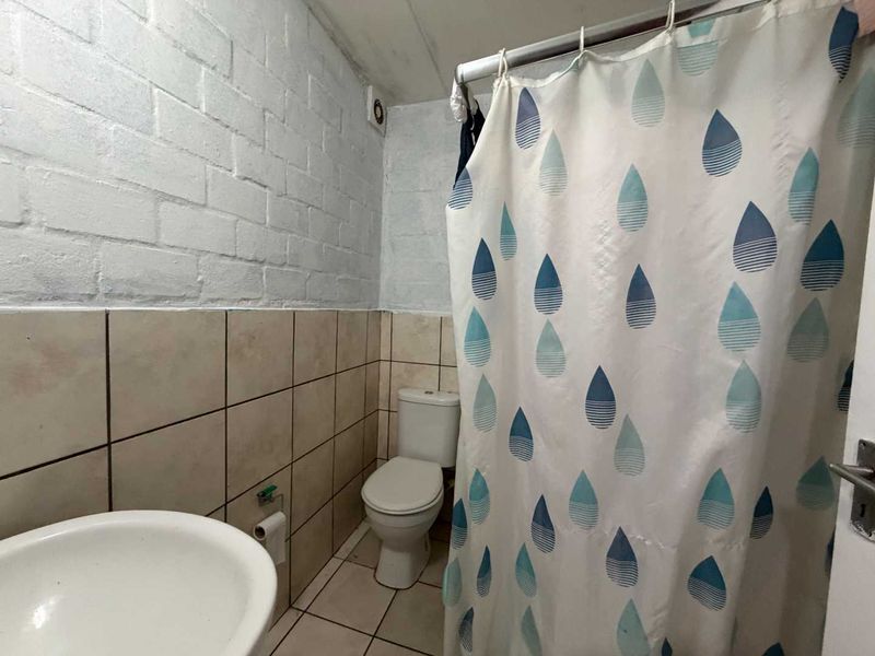 A functional bathroom featuring a toilet, washbasin, and shower area with tiled finishes and painted brick walls.