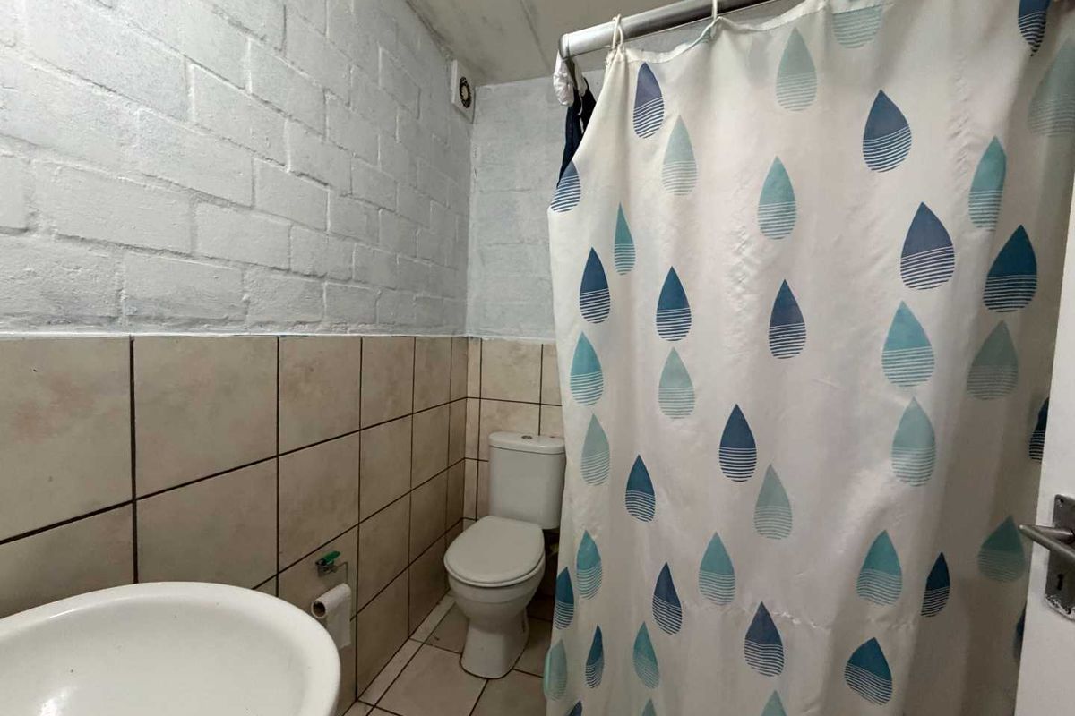 A functional bathroom featuring a toilet, washbasin, and shower area with tiled finishes and painted brick walls.
