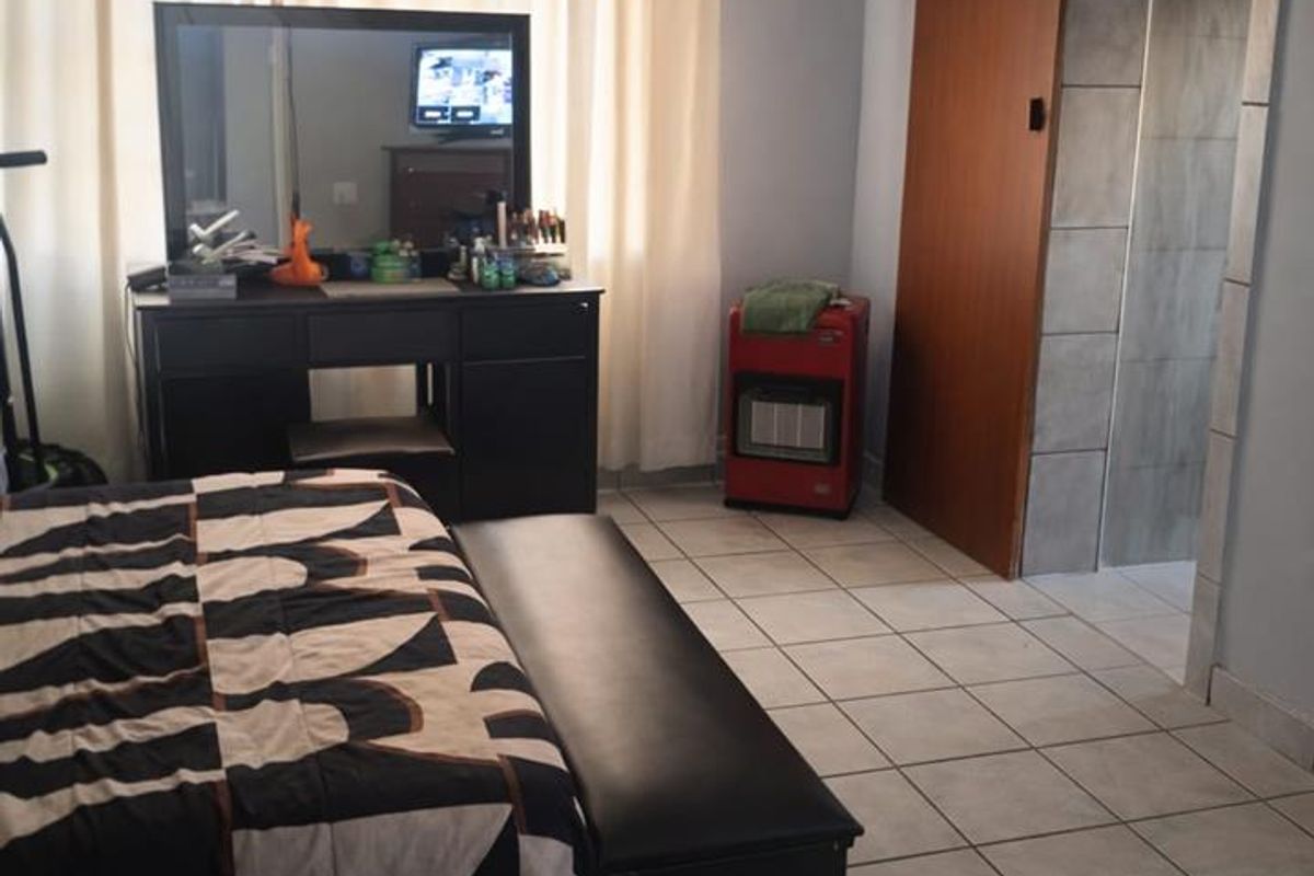 A bedroom featuring tiled flooring, a wall-mounted air conditioning unit, and an adjoining tiled bathroom area with a sliding door.