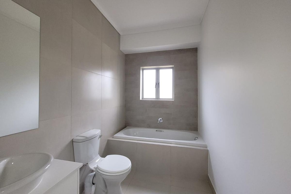 A modern bathroom featuring neutral wall tiles, a built-in bathtub, a white toilet, and a vanity with a basin.