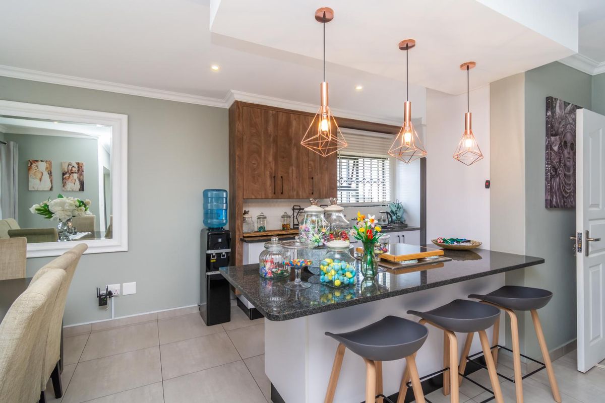 Modern kitchen featuring a granite-topped breakfast island, contemporary pendant lighting, and wood-finish cabinetry, creating a functional and stylish culinary space.