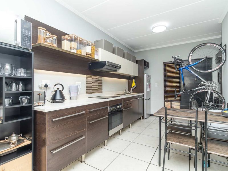 Modern galley-style kitchen featuring dark wood cabinetry, integrated appliances, sleek countertops, and tiled flooring, offering a functional and contemporary cooking space.