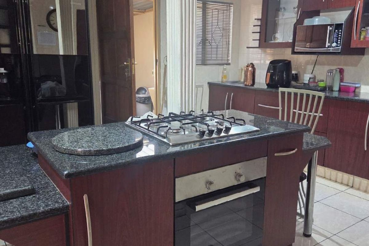 A functional kitchen featuring dark wood cabinetry, granite countertops, a central island with a built-in gas hob and oven, and ceramic floor tiling.