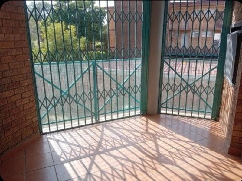 A covered patio area featuring tiled flooring, brick walls, and secure metal security gates.