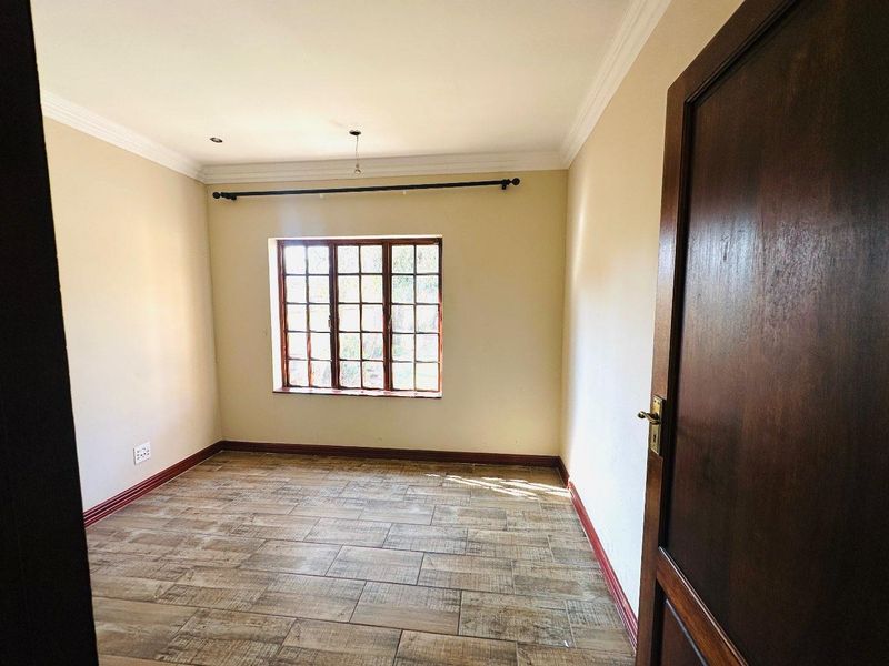 A vacant bedroom featuring tiled flooring, wooden window frames, and classic cornice detailing, offering a clean and neutral space ready for personalization.