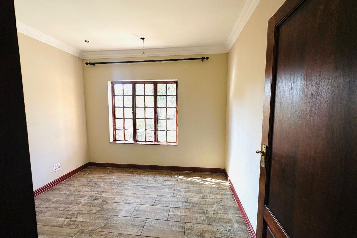 A vacant bedroom featuring tiled flooring, wooden window frames, and classic cornice detailing, offering a clean and neutral space ready for personalization.
