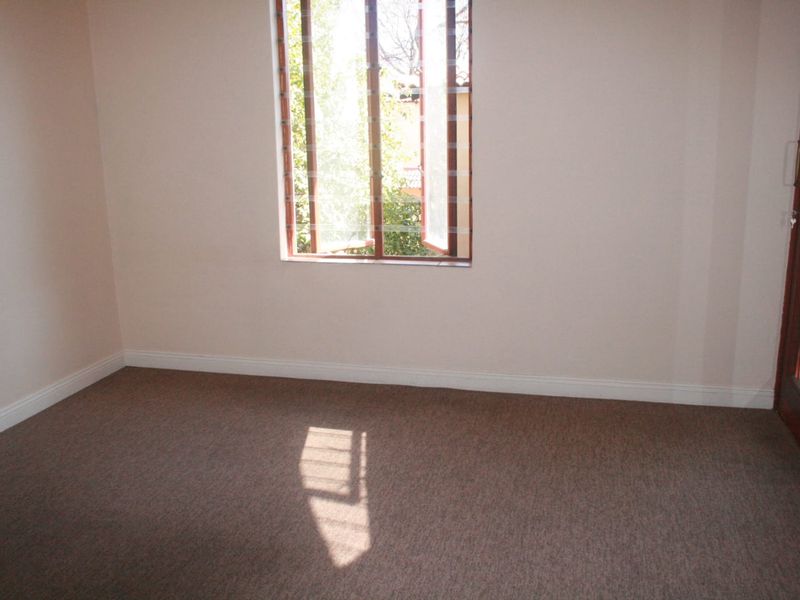 A vacant bedroom featuring neutral wall tones, carpeted flooring, and a window with security bars, offering a clean canvas for personalization.