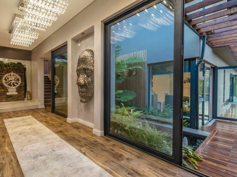 Elegant entrance hall featuring high-end finishes, crystal chandeliers, and large glass doors opening onto a timber deck with a tranquil water feature.