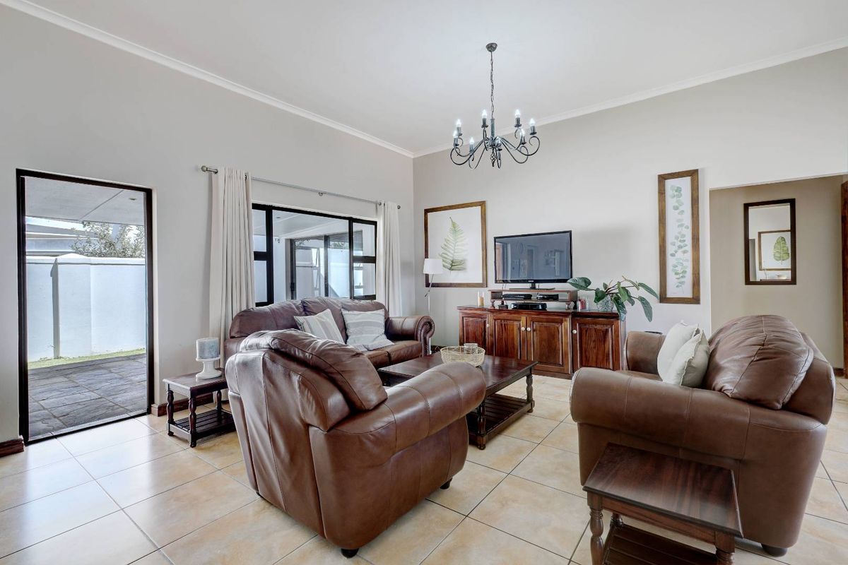 A well-maintained living room featuring tiled flooring, a decorative chandelier, and large glass doors providing access to the outdoor patio area.