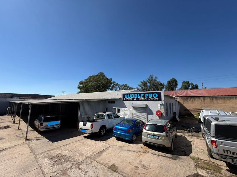 Front exterior view of a commercial workshop featuring a concrete driveway, covered parking area, and roller shutter door access.