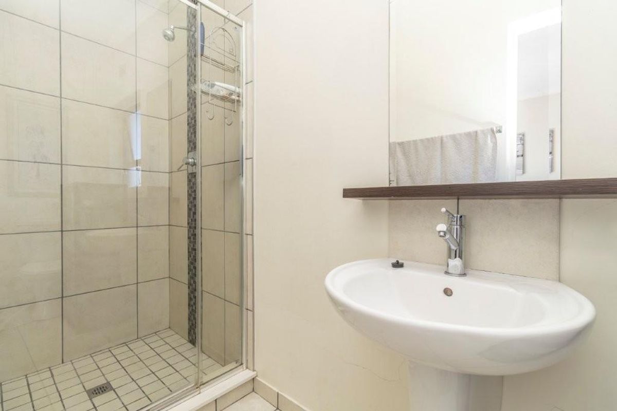 A functional bathroom featuring a glass-enclosed shower, pedestal sink, and wall-mounted mirror with a floating shelf.