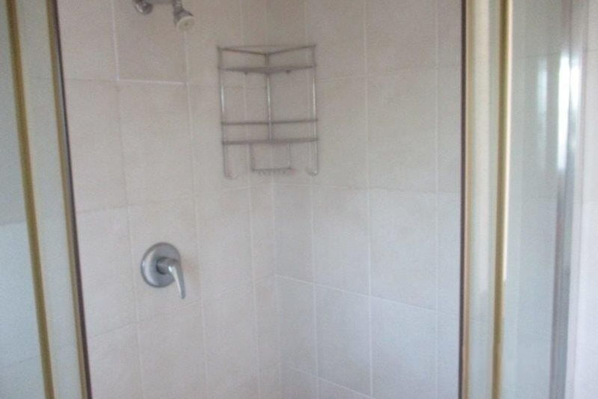 A functional shower enclosure featuring tiled walls, a single-lever mixer tap, and a fixed shower head.