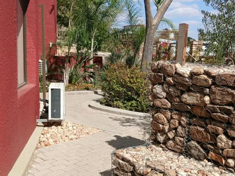 A well-maintained rear exterior area featuring a paved walkway, decorative gabion stone wall, and established garden landscaping.