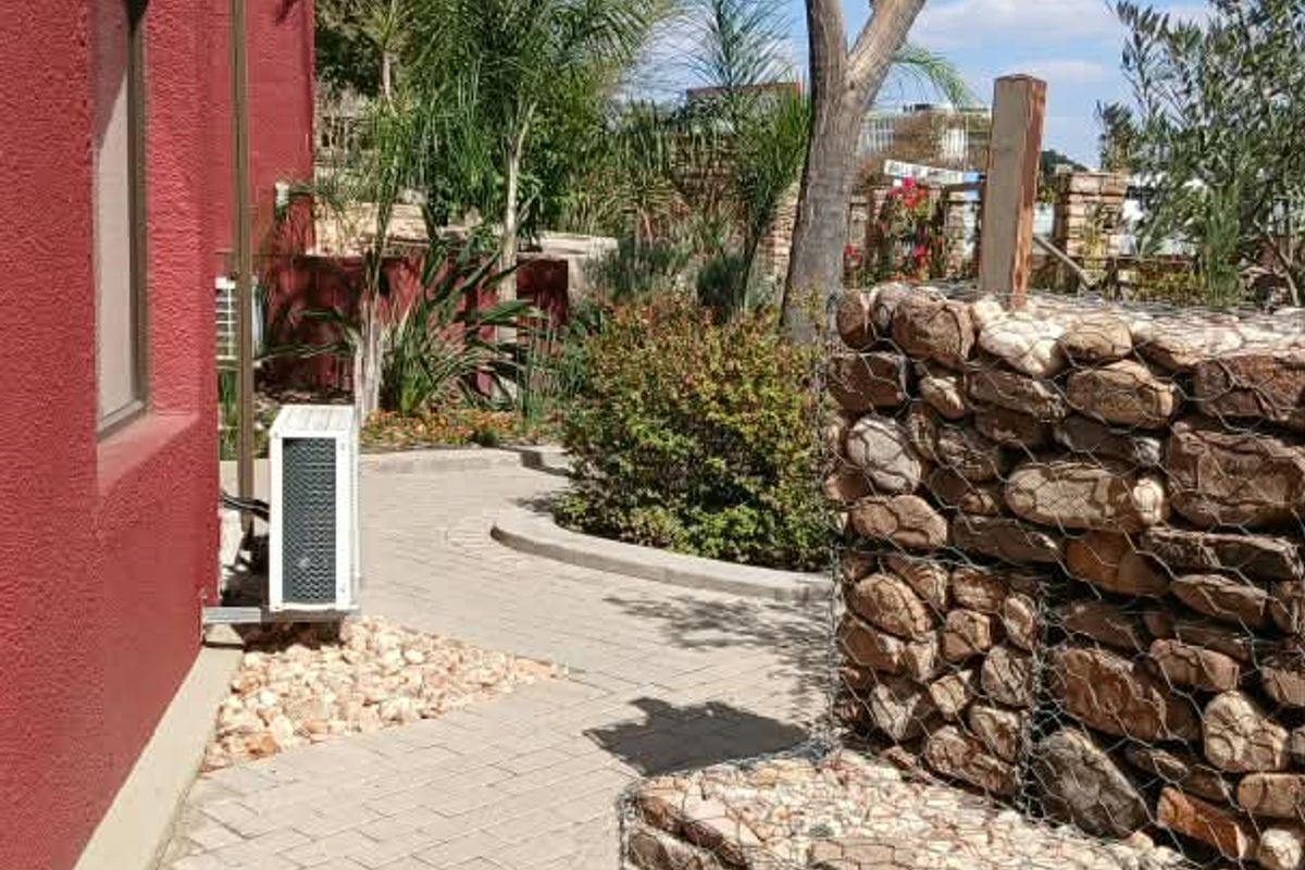A well-maintained rear exterior area featuring a paved walkway, decorative gabion stone wall, and established garden landscaping.