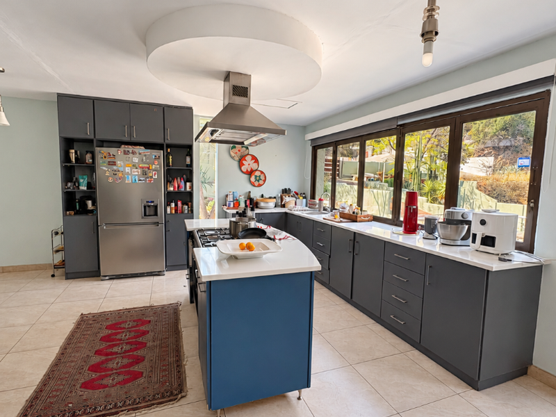 Modern kitchen featuring a central island with gas hob, dark grey cabinetry, stone countertops, and large windows providing ample natural light.