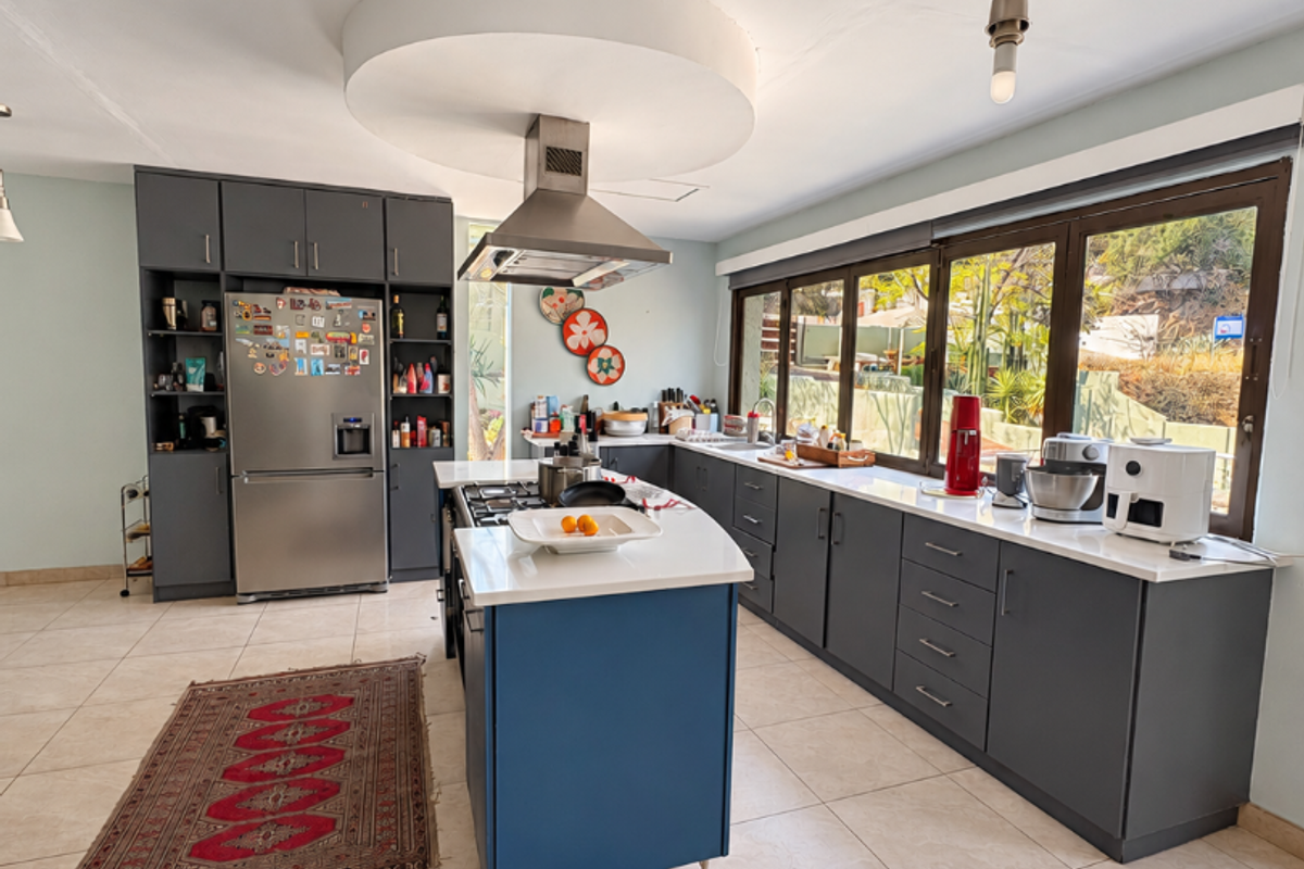 Modern kitchen featuring a central island with gas hob, dark grey cabinetry, stone countertops, and large windows providing ample natural light.