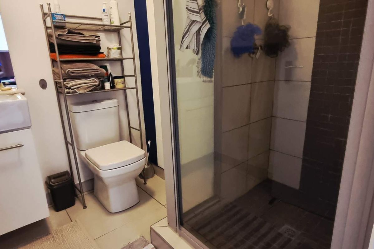 A functional bathroom featuring a vanity basin, a toilet, and a glass-enclosed shower with tiled walls.