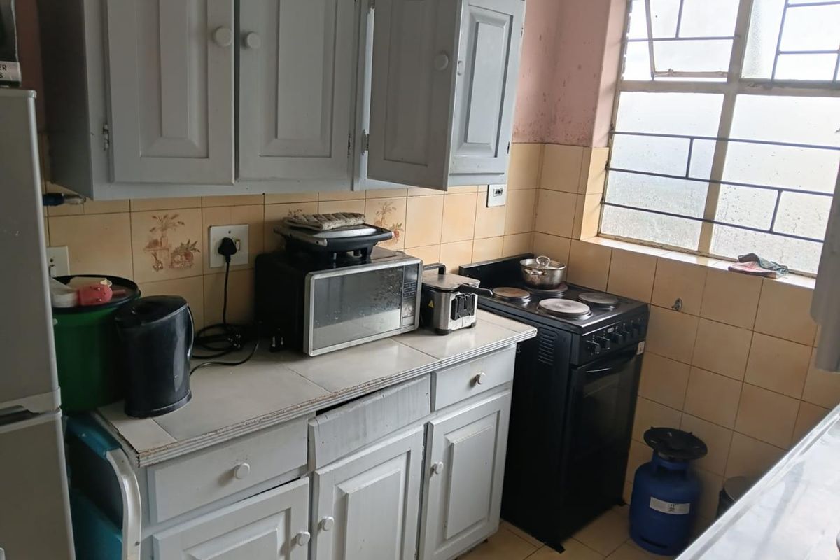A compact kitchen featuring dated cabinetry, tiled countertops, and a built-in electric stove, requiring cosmetic updates to modernize the space.