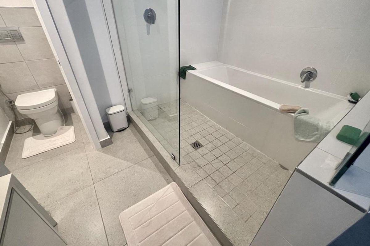 Modern bathroom featuring a glass-enclosed shower and bathtub combination, tiled flooring, and a wall-mounted toilet.