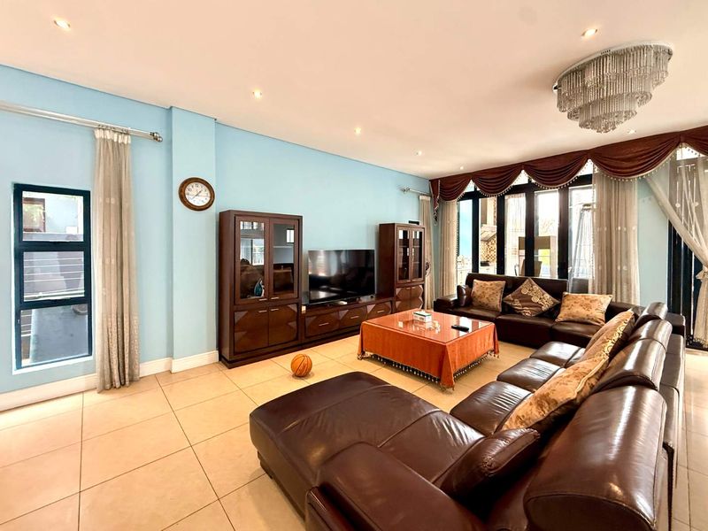 Spacious living room featuring tiled flooring, recessed downlighting, a decorative crystal chandelier, and large aluminium-framed sliding doors providing access to the exterior.