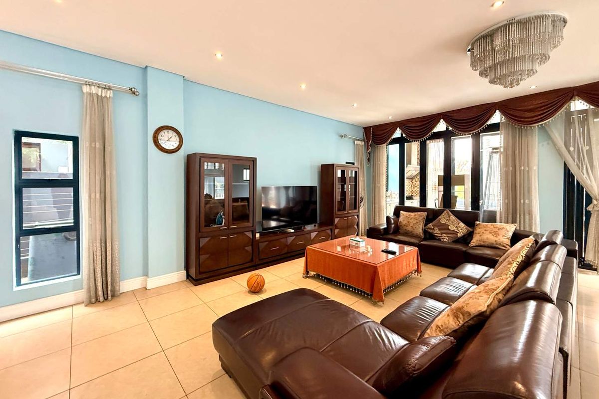Spacious living room featuring tiled flooring, recessed downlighting, a decorative crystal chandelier, and large aluminium-framed sliding doors providing access to the exterior.