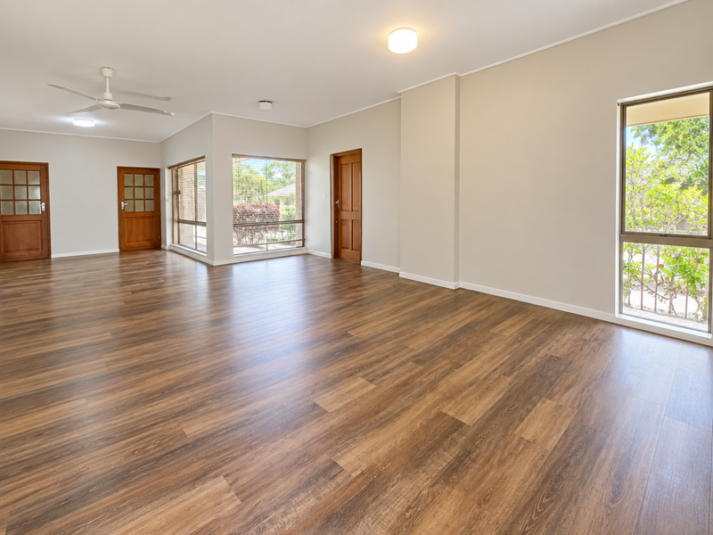 Spacious, light-filled living area featuring modern laminate wood flooring, neutral walls, and large windows providing ample natural light and garden views.