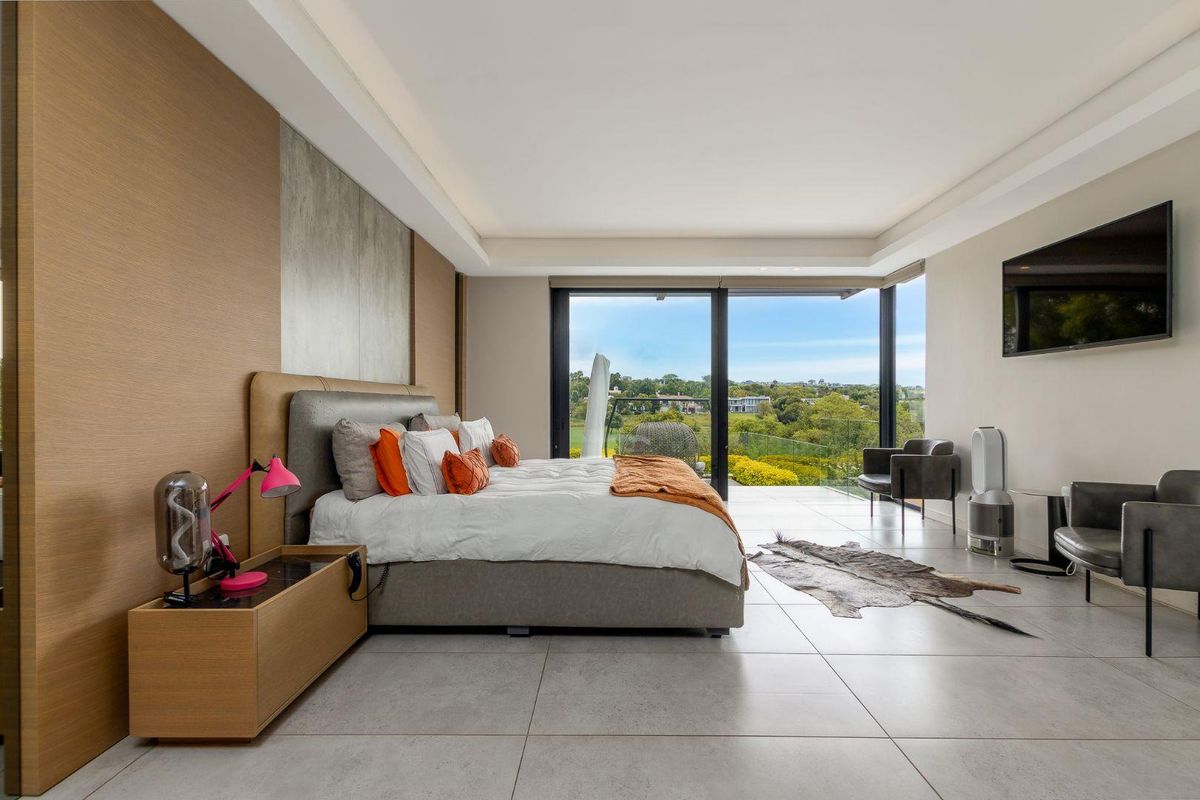 Spacious modern bedroom featuring large sliding glass doors, neutral tiled flooring, recessed ceiling lighting, and an integrated wall-mounted television.